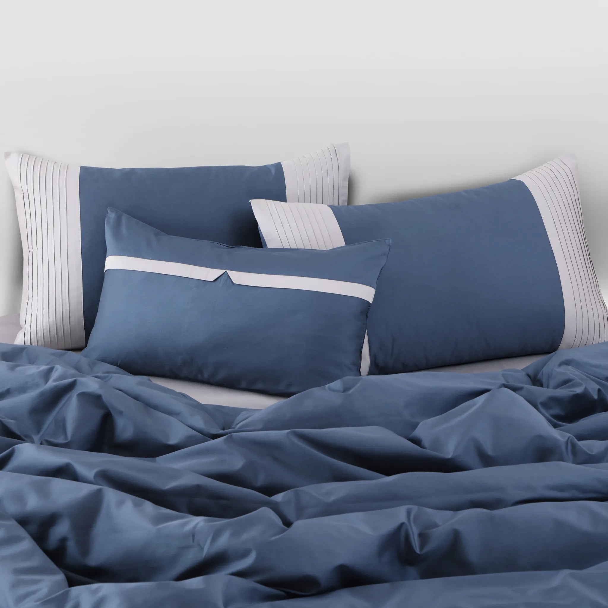 Blue bedding set with white stripes on a bed against a light gray wall.
