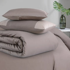 Brown bedding set with pillows and duvet on a bed, with a plant in the background.