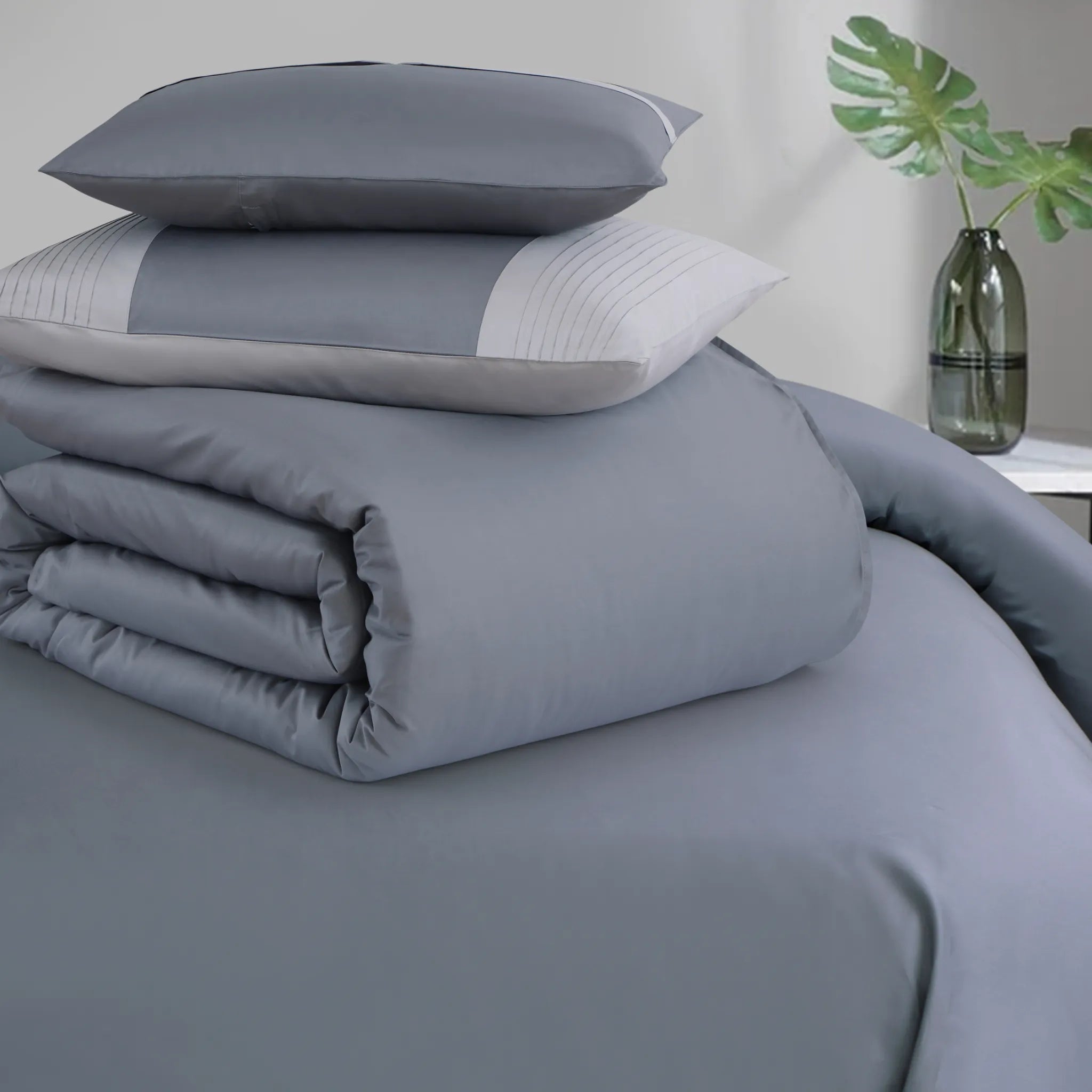 Gray bedding set with pillows on a bed in a bedroom setting.