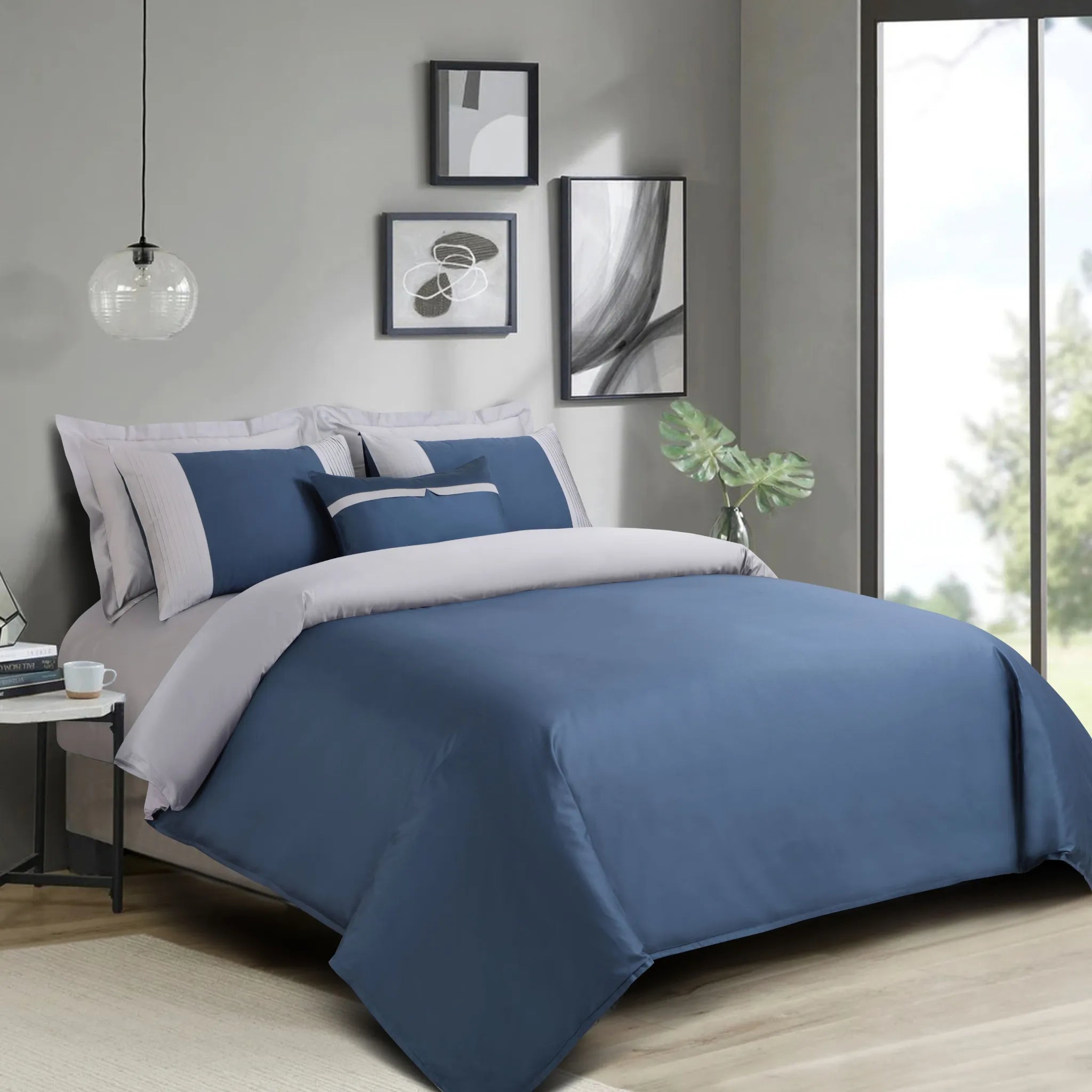 Blue and gray bedding set on a bed in a modern bedroom with light gray walls and large windows.