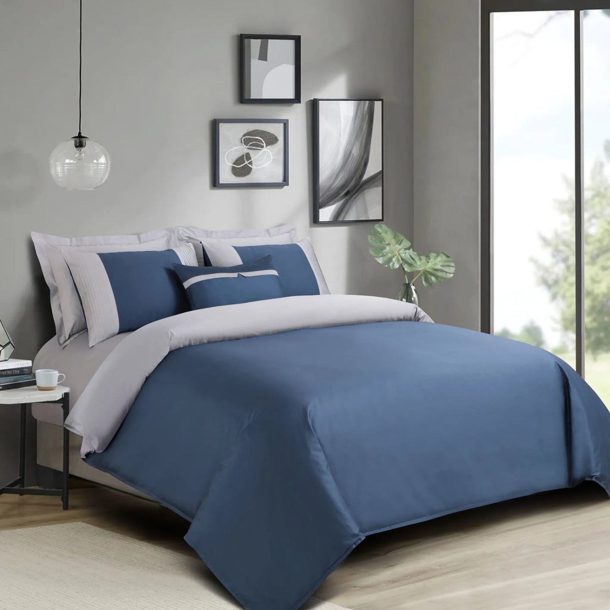 Blue and gray bedding set on a bed in a modern bedroom with light gray walls and large windows.