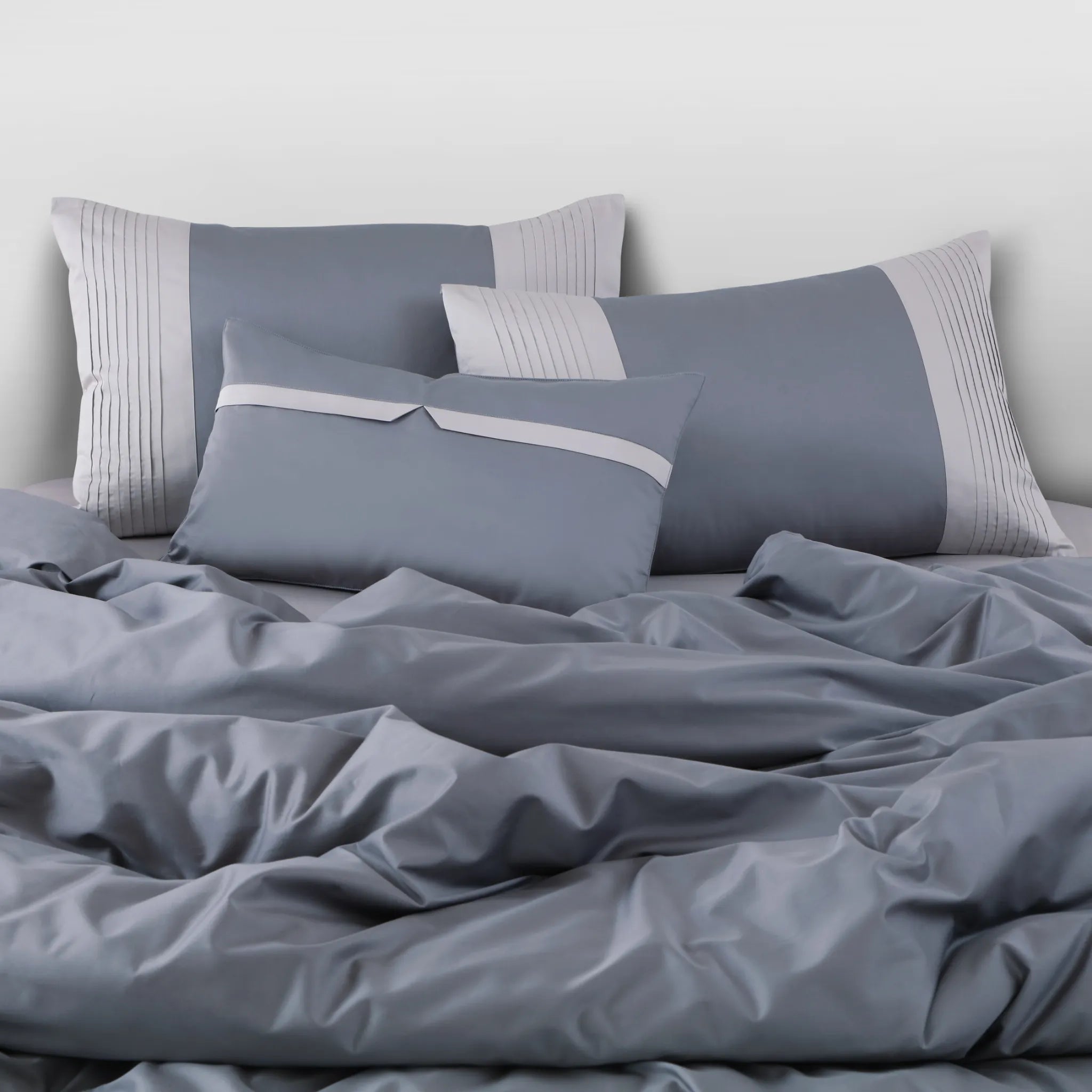 Gray bedding set with pillows on a bed against a white wall