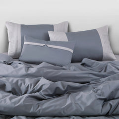 Gray bedding set with pillows on a bed against a white wall