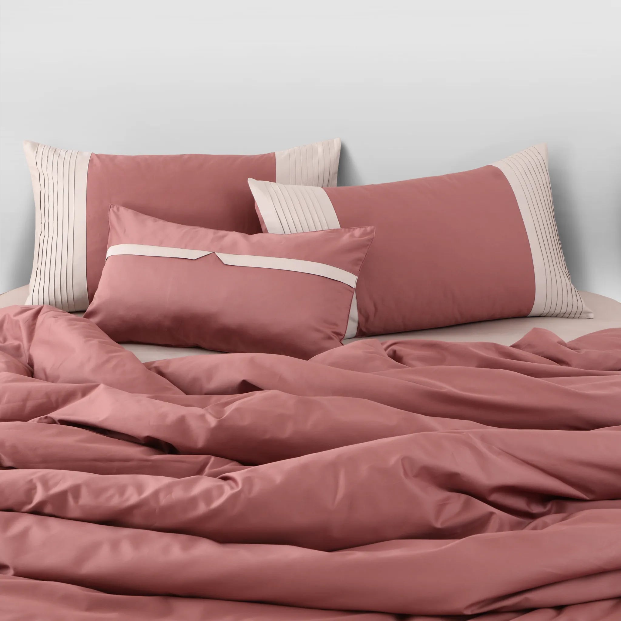 Pink bedding set with matching pillows on a bed against a light gray wall.