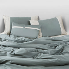Teal bedding set with matching pillows on a bed against a light gray wall.